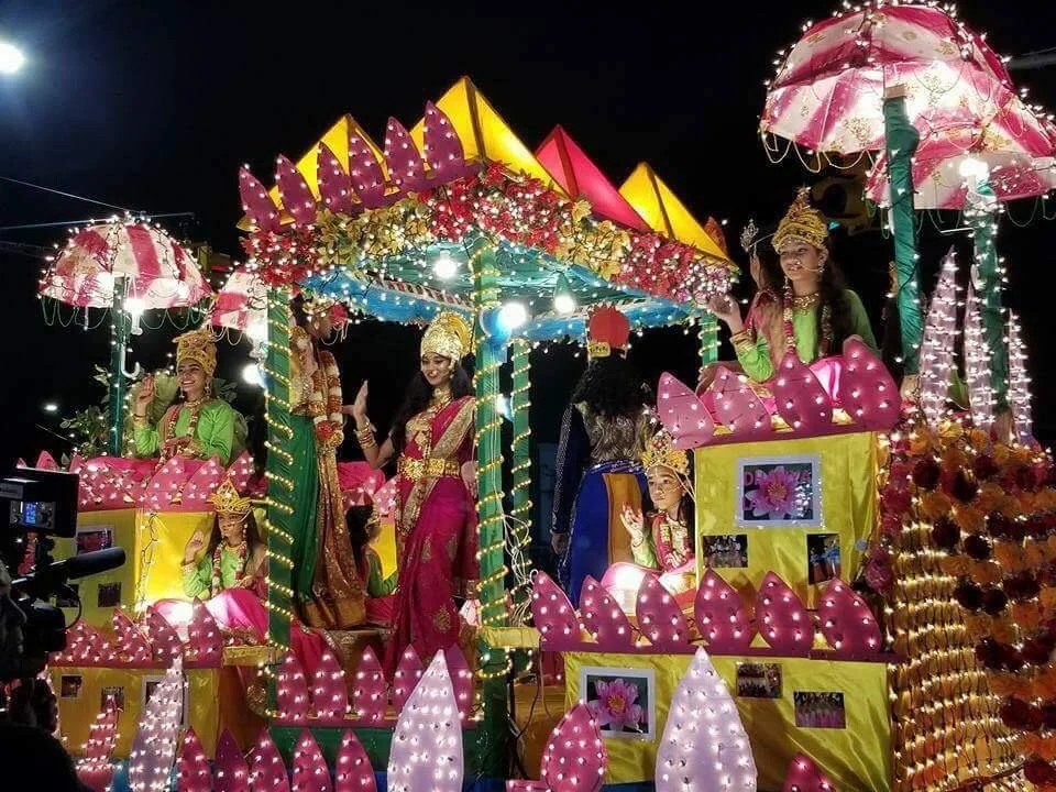 Updated home 2 An illuminated Diwali float decorated with lotus petals, lights, flowers and performers in ceremonial dress.