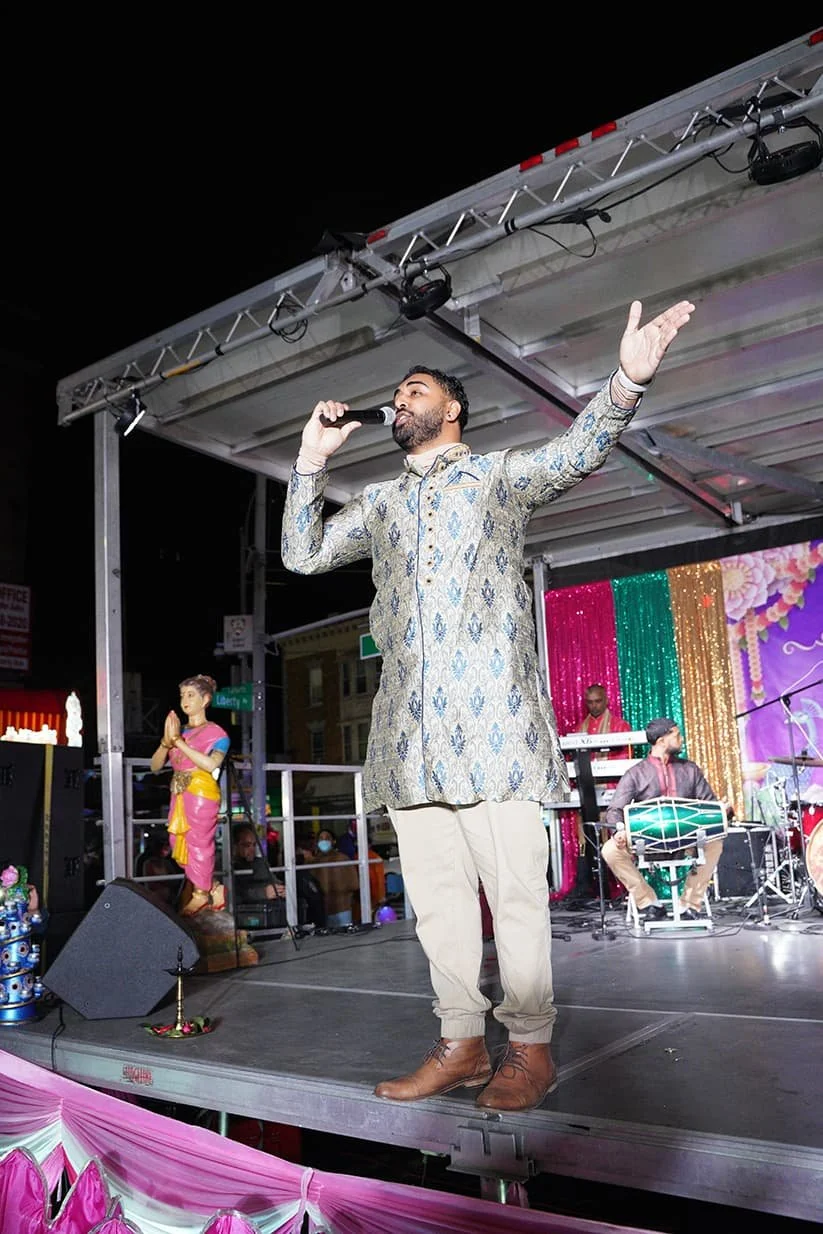 Updated home 7 A singer holds a microphone and raises one arm while performing on the festival stage at night.