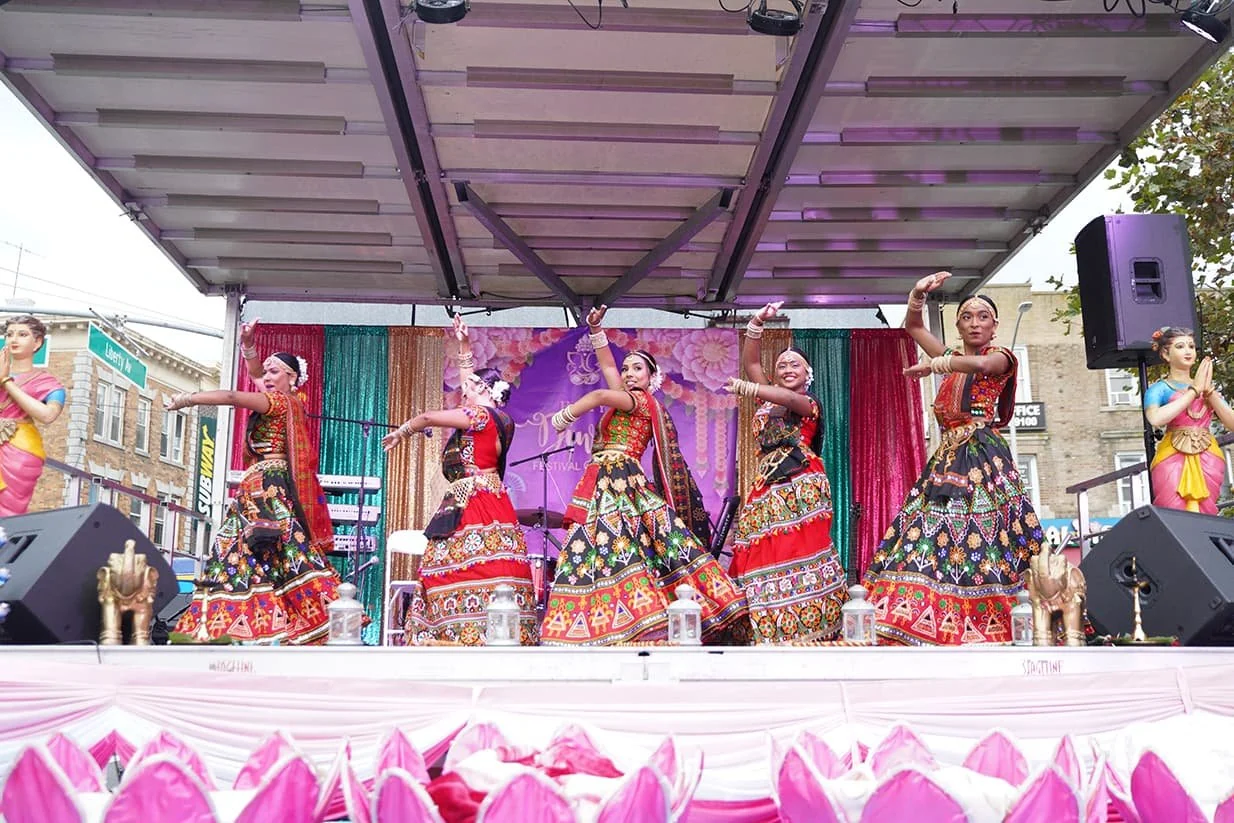 Updated home 6 Dancers in embroidered red and black costumes perform together on the outdoor festival stage.
